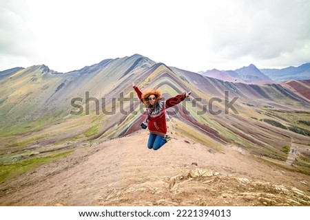 Young red haired smiling girl jumping in front of the Vinicunca Rainbow Mountain, Peru