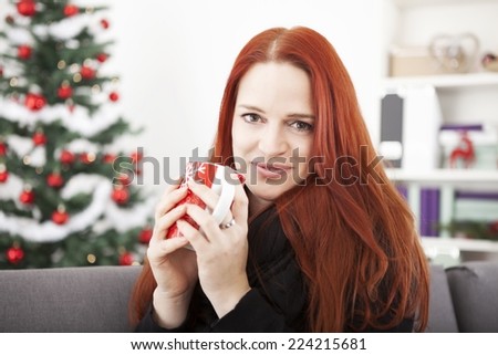young red haired woman is drinking coffee or tea on christmas eve or winter morning