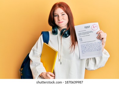 Young Red Head Girl Wearing Student Backpack Holding Passed Test Puffing Cheeks With Funny Face. Mouth Inflated With Air, Catching Air. 