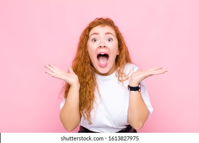 young red head woman feeling shocked and excited, laughing, amazed and happy because of an unexpected surprise against pink wall - Shutterstock ID 1613827975
