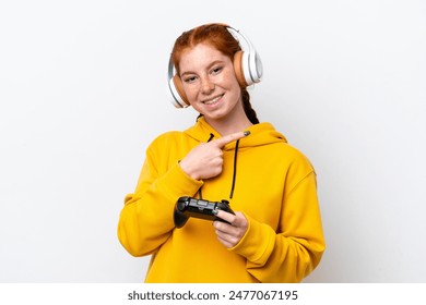 Young reddish woman playing with a video game controller isolated on white background pointing back - Powered by Shutterstock