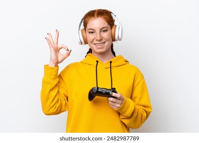 Young reddish woman playing with a video game controller isolated on white background showing ok sign with fingers - Powered by Shutterstock