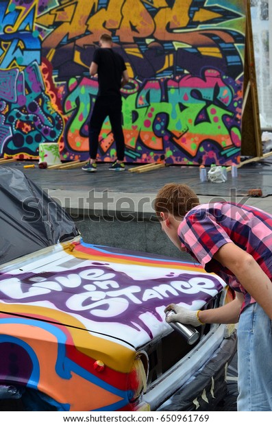 A young red-haired graffiti artist paints a new\
colorful graffiti on the car. Photo of the process of drawing a\
graffiti on a car close-up. The concept of street art and illegal\
vandalism