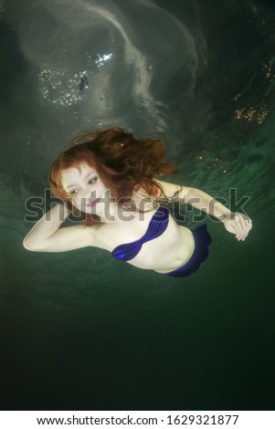 Young red-haired mermaid swims underwater