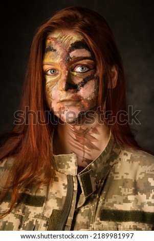Young red-haired woman with camouflage makeup on a dark background