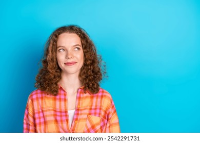 Young redhaired woman in casual plaid shirt posing with thoughtful and happy expression against bright blue background - Powered by Shutterstock