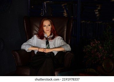 A Young Red-haired Woman With A Haughty Expression On Face Sitting In An Old Library In Leather Chair. She Is Dressed In A White Shirt, Black Skirt And Green Tie. Mafia Princess, Librarian Or Whitch.