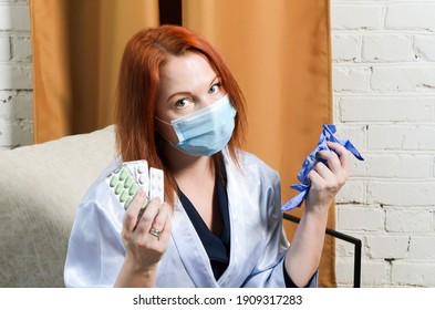 Young Red-haired Woman In Medical Mask Holds Pills And Rubber Gloves In Her Hands. Concept: Quarantined Coronavirus Treatment, Illness, Outpatient Treatment, Medications.