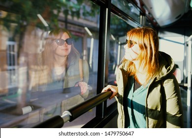 A Young Red-haired Woman In Sun Glasses Looking At Her Reflection In A Bus Window