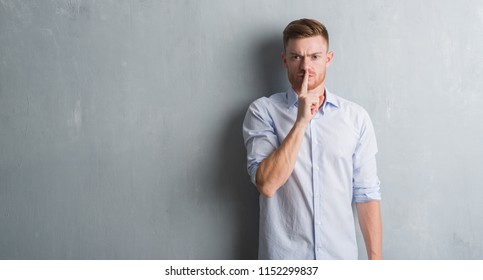 Young redhead business man over grey grunge wall asking to be quiet with finger on lips. Silence and secret concept. - Shutterstock ID 1152299837