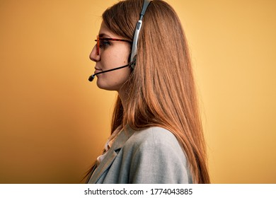 Young redhead call center agent woman overworked wearing glasses using headset looking to side, relax profile pose with natural face with confident smile.