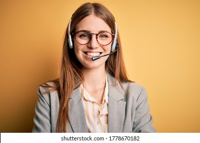 Young redhead call center agent woman overworked wearing glasses using headset happy face smiling with crossed arms looking at the camera. Positive person.