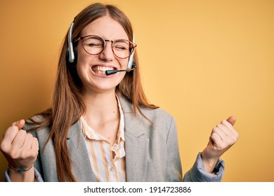 Young redhead call center agent woman overworked wearing glasses using headset very happy and excited doing winner gesture with arms raised, smiling and screaming for success. Celebration concept.