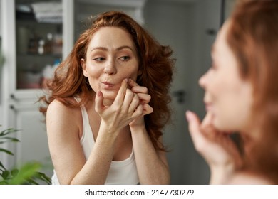 Young redhead caucasian woman in the bathroom having acne problems with face