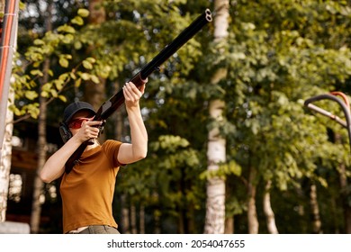Young redhead caucasian woman on tactical gun training classes. Woman with weapon. Outdoor Shooting Range. Side view on beautiful lady with rifle machine gun in the forest, slim female is hunting