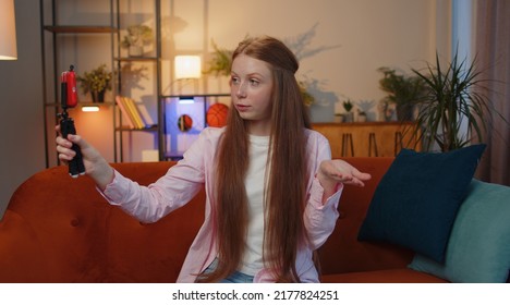 Young Redhead Child Girl Blogger Taking Selfie On Smartphone Selfie Stick, Communicating Video Call Online With Subscribers. Teen Freckles Kid At Modern Home Apartment Living Room Sitting On Couch