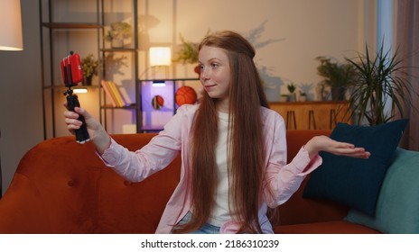 Young Redhead Child Girl Blogger Taking Selfie On Smartphone Selfie Stick, Communicating Video Call Online With Subscribers. Teen Freckles Kid At Modern Home Apartment Living Room Sitting On Couch