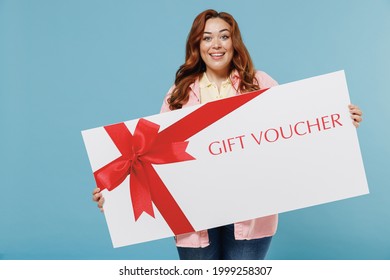 Young Redhead Chubby Overweight Woman 30s With Curly Hair Wear Casual Pink Shirt Hold Big Gift Certificate Coupon Voucher Card For Store Isolated On Pastel Blue Background People Lifestyle Concept.