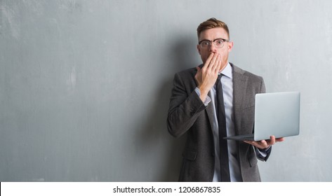 Young Redhead Elegant Business Man Over Grey Grunge Wall Using Laptop Cover Mouth With Hand Shocked With Shame For Mistake, Expression Of Fear, Scared In Silence, Secret Concept