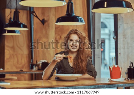 Young redhead female eating spicy noodles in an Asian restaurant. 