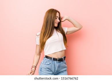 Young Redhead Ginger Woman Against A Pink Wall Dancing And Having Fun.