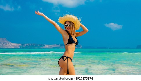 Junge Rotkopfmädchen in schwarzem Bikini und mit Hut auf Balos Strand, West Kreta, Griechenland. Sommerurlaub, Juli