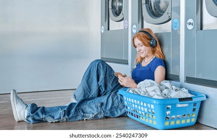 Young redhead girl in a public laundry sitting on the floor listening to music while waiting for clothes to be washed - Powered by Shutterstock