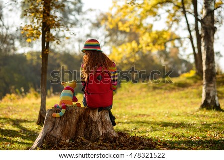 Young redhead girl sitting on stump with her alive toy cat and dreaming