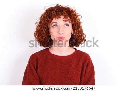 young redhead girl wearing red sweater over white background making fish face with lips, crazy and comical gesture. Funny expression.