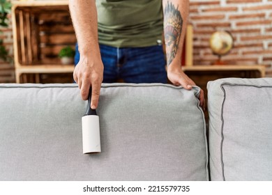 Young Redhead Man Cleaning Sofa Using Pet Hair Roller At Home