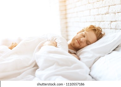 Young redhead man sleeps under white blanket. Sweet dreams. Waking up. Healthy sleep.