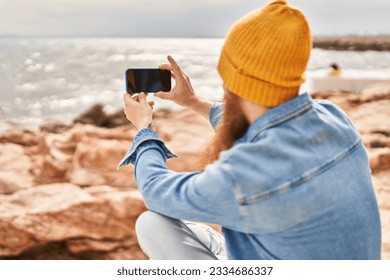 Young redhead man standing on back view make photo by smartphone at seaside - Powered by Shutterstock