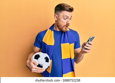 Young Redhead Man Wearing Hooligan Scarf And Using Smartphone Afraid And Shocked With Surprise And Amazed Expression, Fear And Excited Face. 