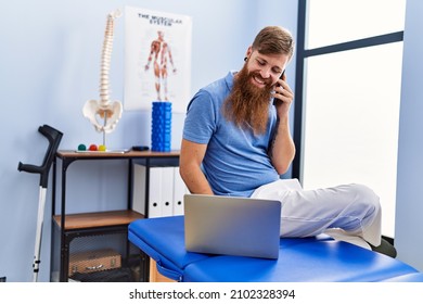 Young redhead man wearing physiotherapist uniform using laptop and talking on the smartphone at physiotherapy clinic - Powered by Shutterstock