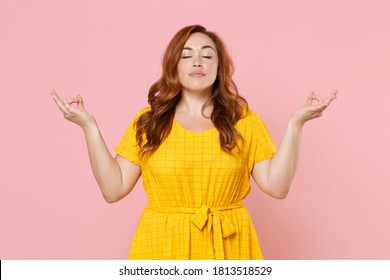 Young Redhead Plus Size Body Positive Woman 20s In Yellow Dress Hold Hands In Yoga Gesture, Relaxing Meditating, Trying To Calm Down Isolated On Pastel Pink Color Background Studio Portrait