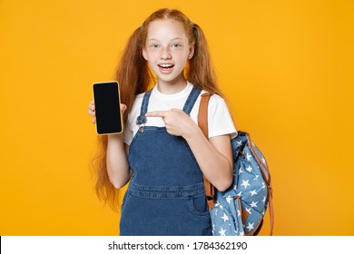 Young Redhead School Teen Girl 12-13 Years Old In White T-shirt Backpack Hold In Hand Using Mobile Cell Phone Isolated On Yellow Background Children Studio Portrait Kids Education Lifestyle Concept.