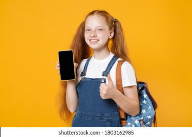 Young Redhead School Teen Girl 12-13 Years Old In White T-shirt Backpack Hold In Hand Using Mobile Cell Phone Isolated On Yellow Background Children Studio Portrait Kids Education Lifestyle Concept.