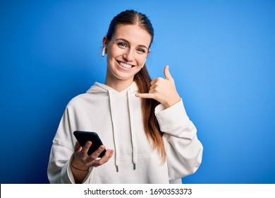 Young Redhead Sportswoman Doing Sport Listening To Music Using Earphones And Smartphone Smiling Doing Phone Gesture With Hand And Fingers Like Talking On The Telephone. Communicating Concepts.