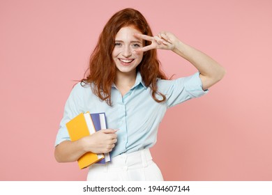 Young redhead student woman in blue shirt hold books notebook cover eye with victory v-sign gesture isolated on pastel pink background studio portrait. Education high school university college concept