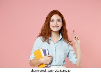 Young Redhead Student Woman In Blue Shirt Hold Book Wait Special Moment Keep Fingers Cross Making Wish Eyes Closed Isolated On Pastel Pink Background Education High School University College Concept