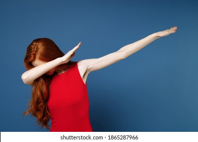 Young Redhead Woman 20s Wearing Bright Red Elegant Evening Dress Standing Doing Dab Hip Hop Dance Hands Gesture, Youth Sign Hiding And Covering Face Isolated On Blue Color Background Studio Portrait