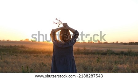 Young redhead woman in beautiful boho dress relaxing in the field during foggy sunset, female outdoors with bouquet in hands	