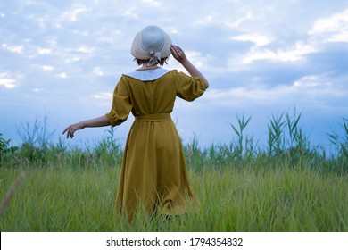 Young redhead woman with  
freckles in vintage handmade dress walk in fields with flowers 