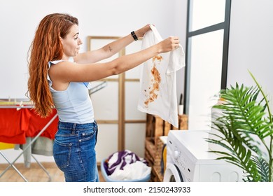 Young Redhead Woman Holding Dirty T Shirt At Laundry Room