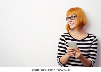 Young Redhead Woman Holding A Mobile Phone Looking To The Left Of The Frame Towards Blank White Copy Space With Smile