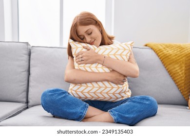 Young redhead woman hugging cushion sitting on sofa at home - Shutterstock ID 2349135403
