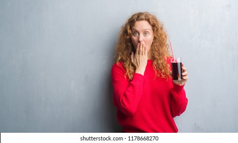 Young Redhead Woman Over Grey Grunge Wall Drinking Soda Refreshment Cover Mouth With Hand Shocked With Shame For Mistake, Expression Of Fear, Scared In Silence, Secret Concept