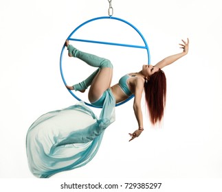 young redhead woman performs acrobatic elements in the air ring on a white background