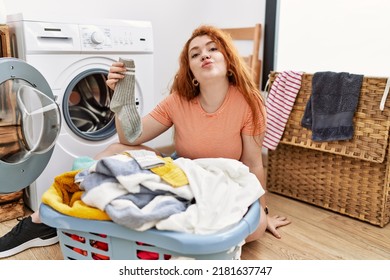 Young Redhead Woman Putting Dirty Laundry Into Washing Machine Looking At The Camera Blowing A Kiss On Air Being Lovely And Sexy. Love Expression. 