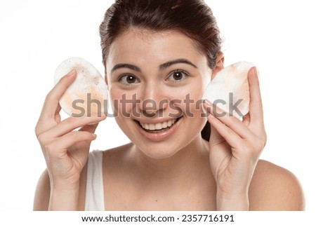 young redhead woman shows a dirty cotton pad of cotton from cleaning her makeup on a white studio background